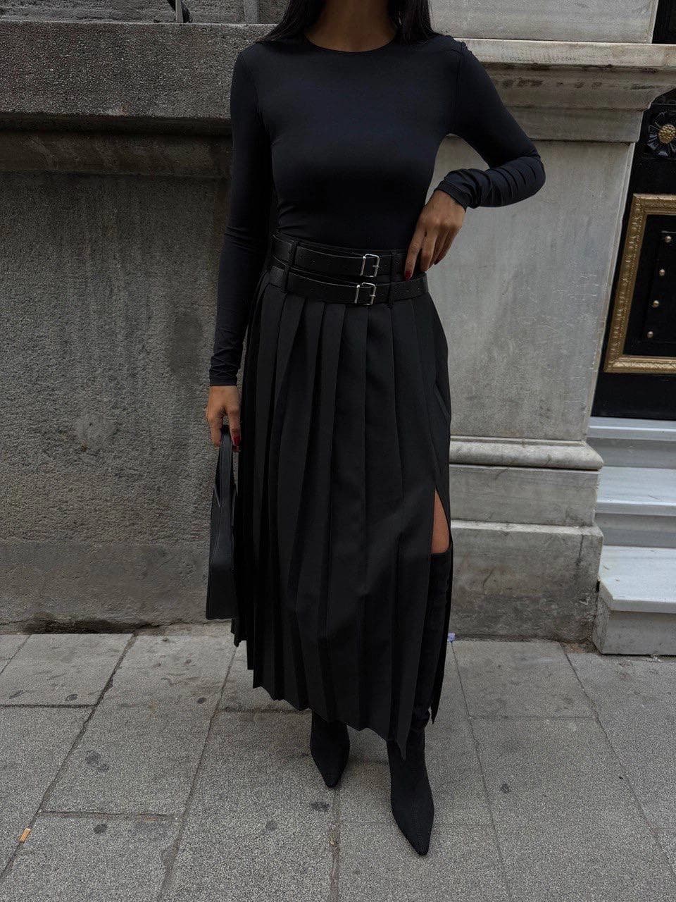 Black high-waisted pleated midi skirt, A-line cut, featuring a double buckle belt and stylish side slit. Modern wool ...