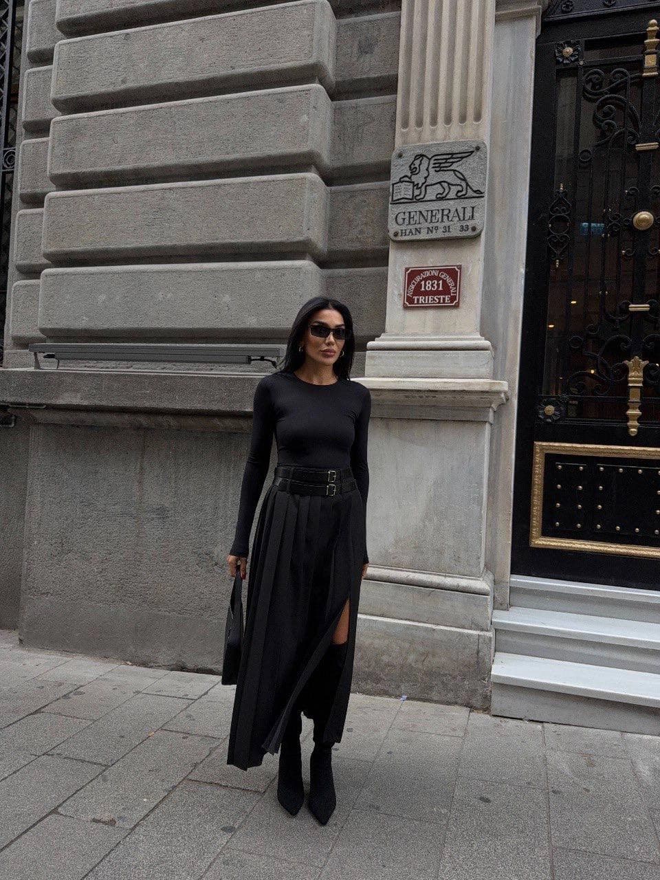 Deep onyx attire piece, long with fine vertical creases, an elevated broad waistband, paired square clasps, and a thi...