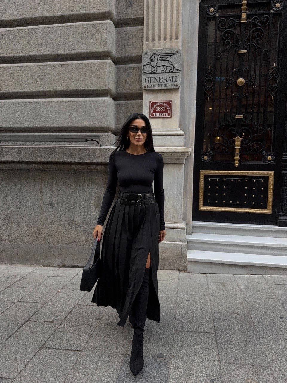 Jet pleated skirt, double buckle, defined waist, a-line silhouette, leg vent, modeled on a woman striding confidently.