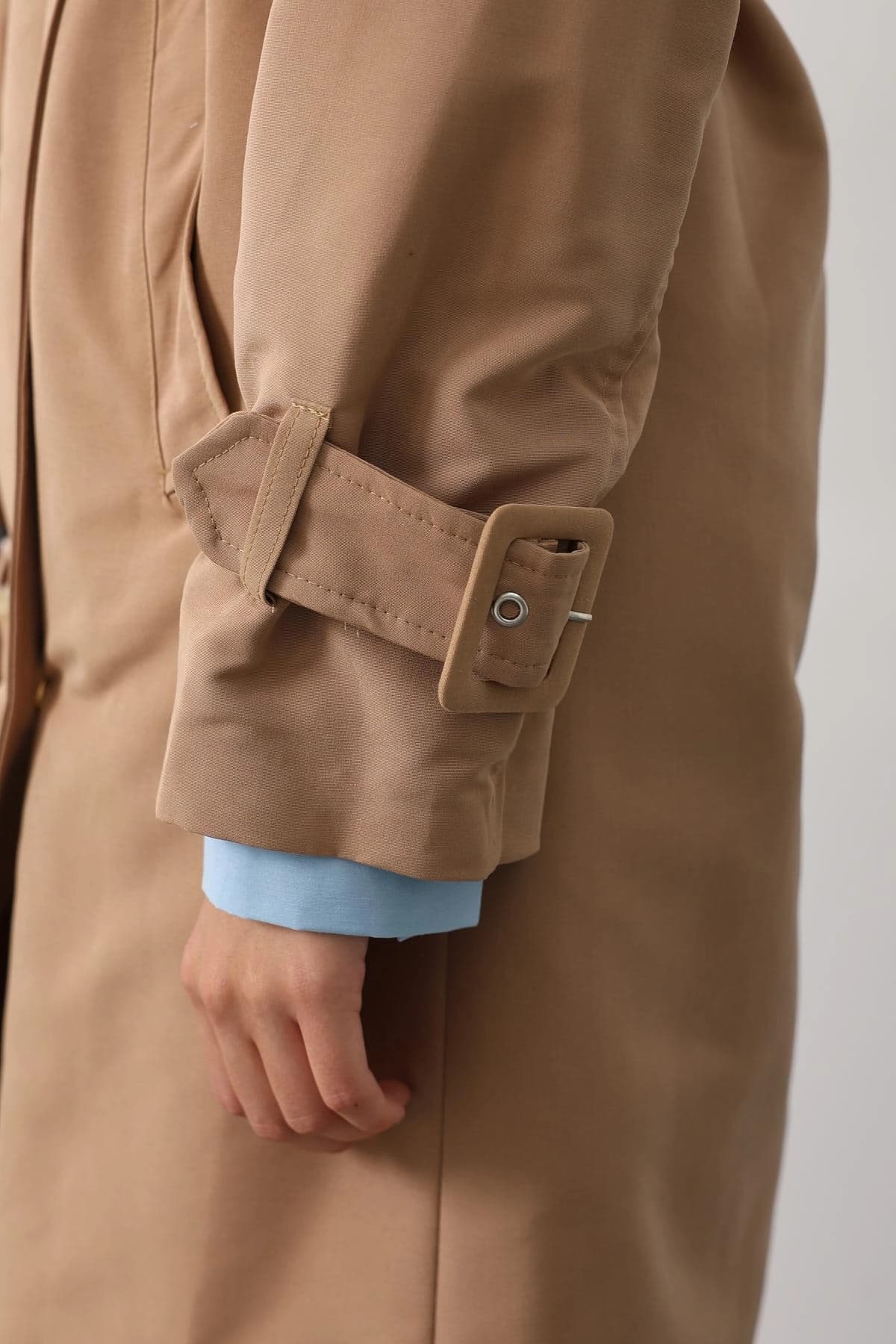 Khaki outerwear's buckled fore-arm accent, complete with metal pin, above a pale blue interior shirt.