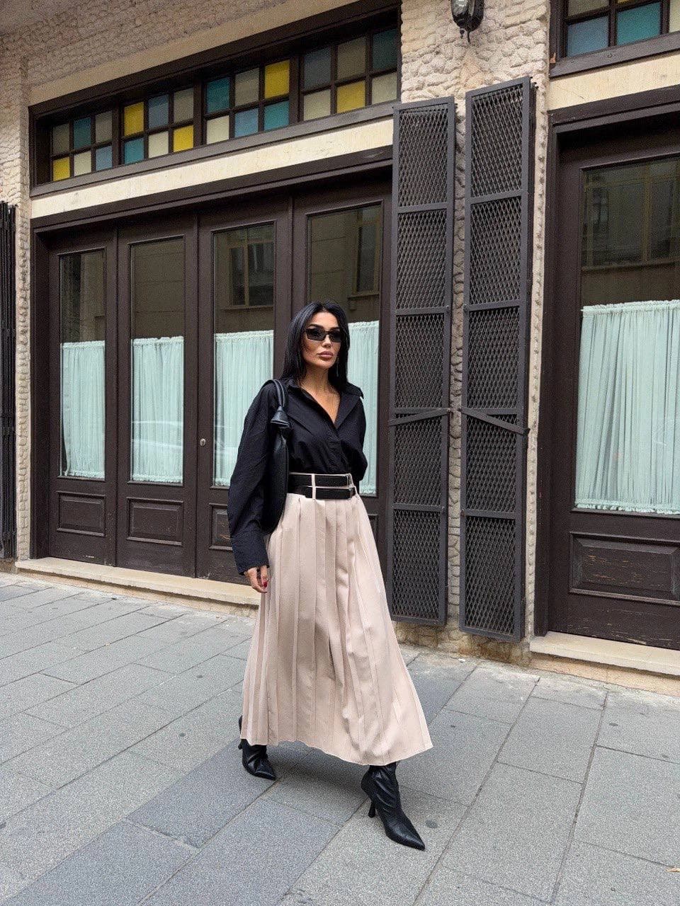 Light fawn ankle-length skirt, precisely pleated, featuring a wide twin-buckle jet-black belt, styled with a sophisti...