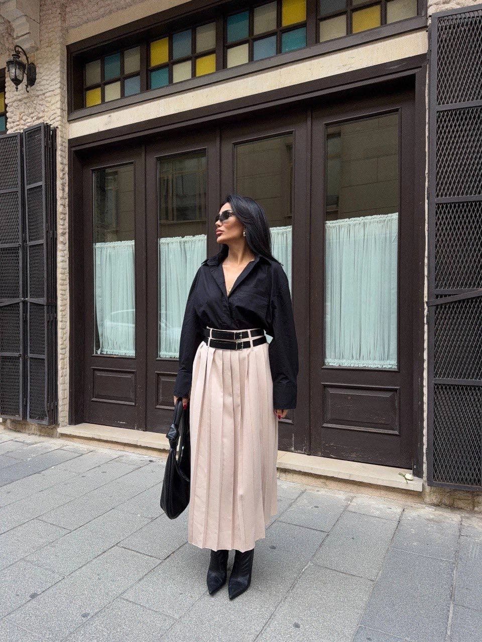 Pale elevated-waist folded mid-length skirt with a dark two-buckle strap, styled with a black long-sleeve top for women.