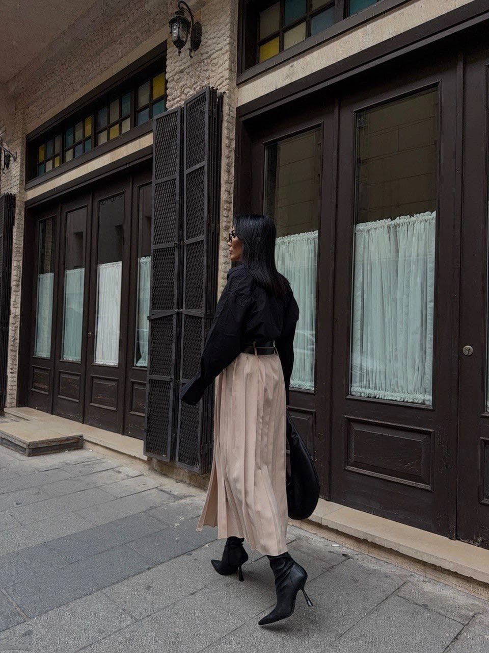 Natural hued garment with sharp accordion creases, calf-length. Displays an onyx dual-buckle waist cincher; worn with...