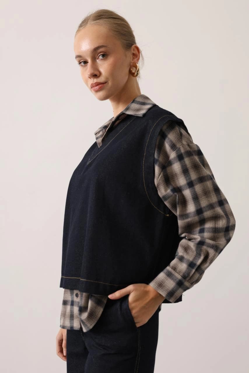 Youthful individual in a dark wash jean waistcoat with a V-shaped opening and gold topstitching, over a beige checked...